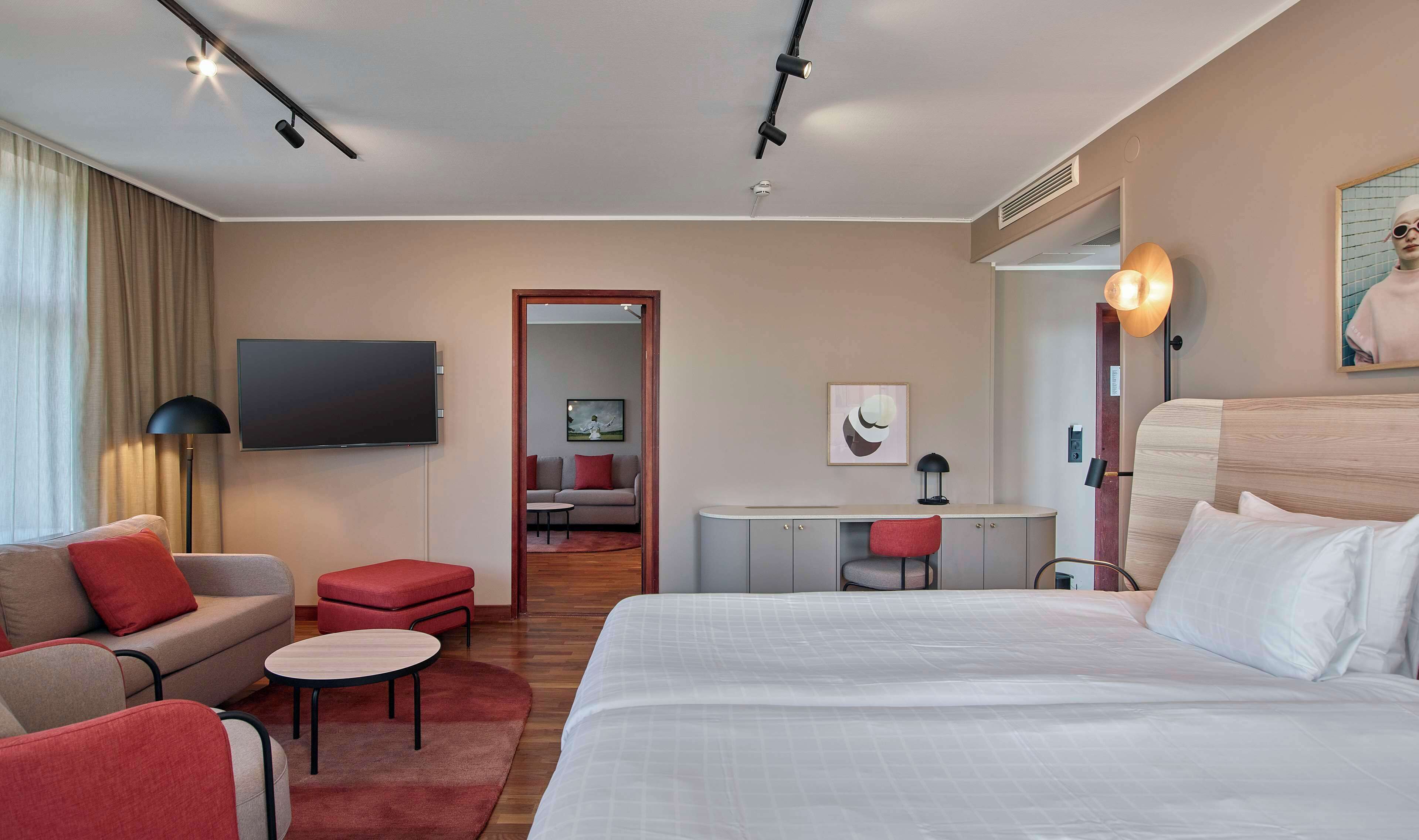 A modern hotel room with a large bed, a sofa, a desk, and a TV.