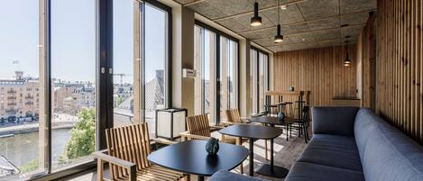 Un interior moderno con ventanas amplias, mobiliario de madera y vistas a un río y edificios.
