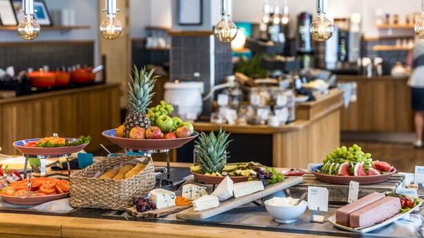 Buffet com diversos alimentos, incluindo frutas, queijos e carnes.