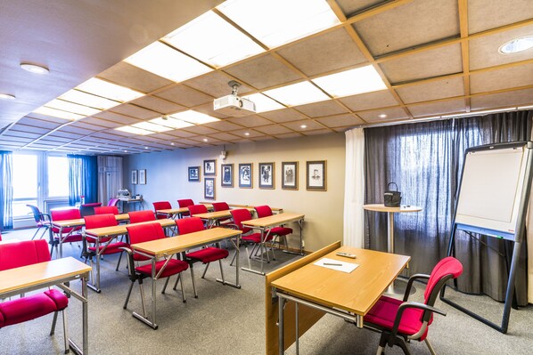 A classroom with desks and chairs, a projector, a whiteboard, and framed pictures on the wall.
