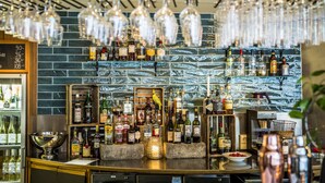 Uma área de bar com diversas garrafas de bebidas, copos e um cardápio em lousa.