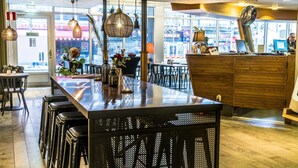 Uma área de bar moderna com um balcão comprido, banquetes, luminárias pendentes e vista para a rua.