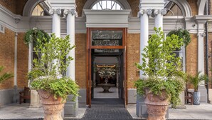 A hotel entrance with a brick facade, large columns, and potted plants. - Oatlands Park Hotel (Weybridge)