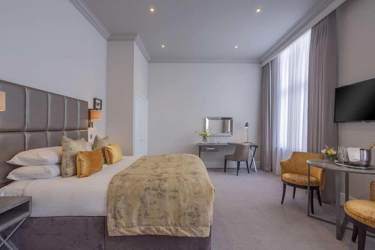 A hotel room with a bed, desk, chair, TV, and large windows.
