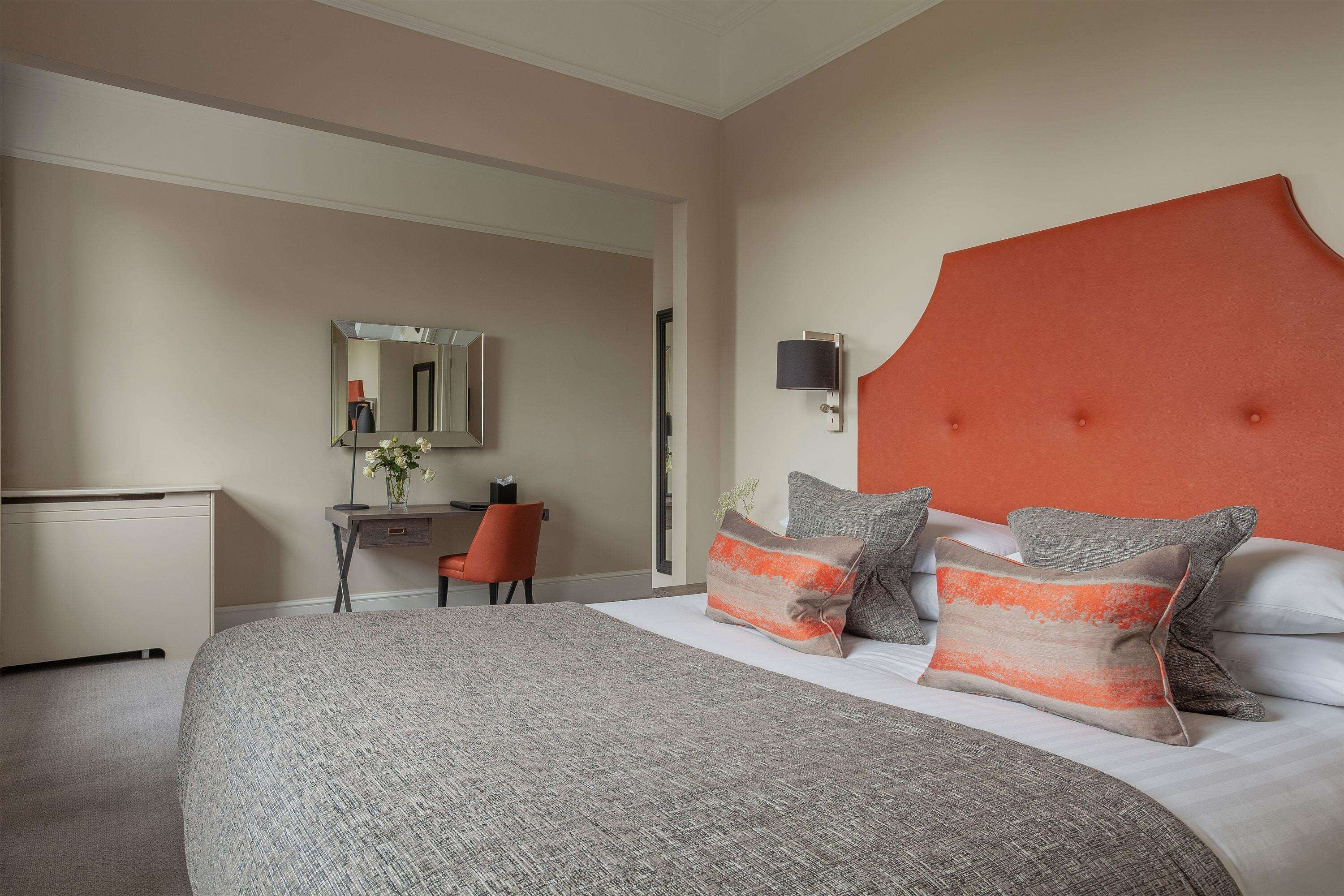 Ein Hotelzimmer mit einem großen Bett, einem Schreibtisch mit Stuhl, einem Spiegel und einer Wandleuchte.