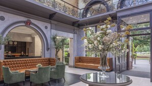 A lobby with a brown leather sofa, green armchairs, a glass coffee table, and a large vase of flowers. - Oatlands Park Hotel (Weybridge)