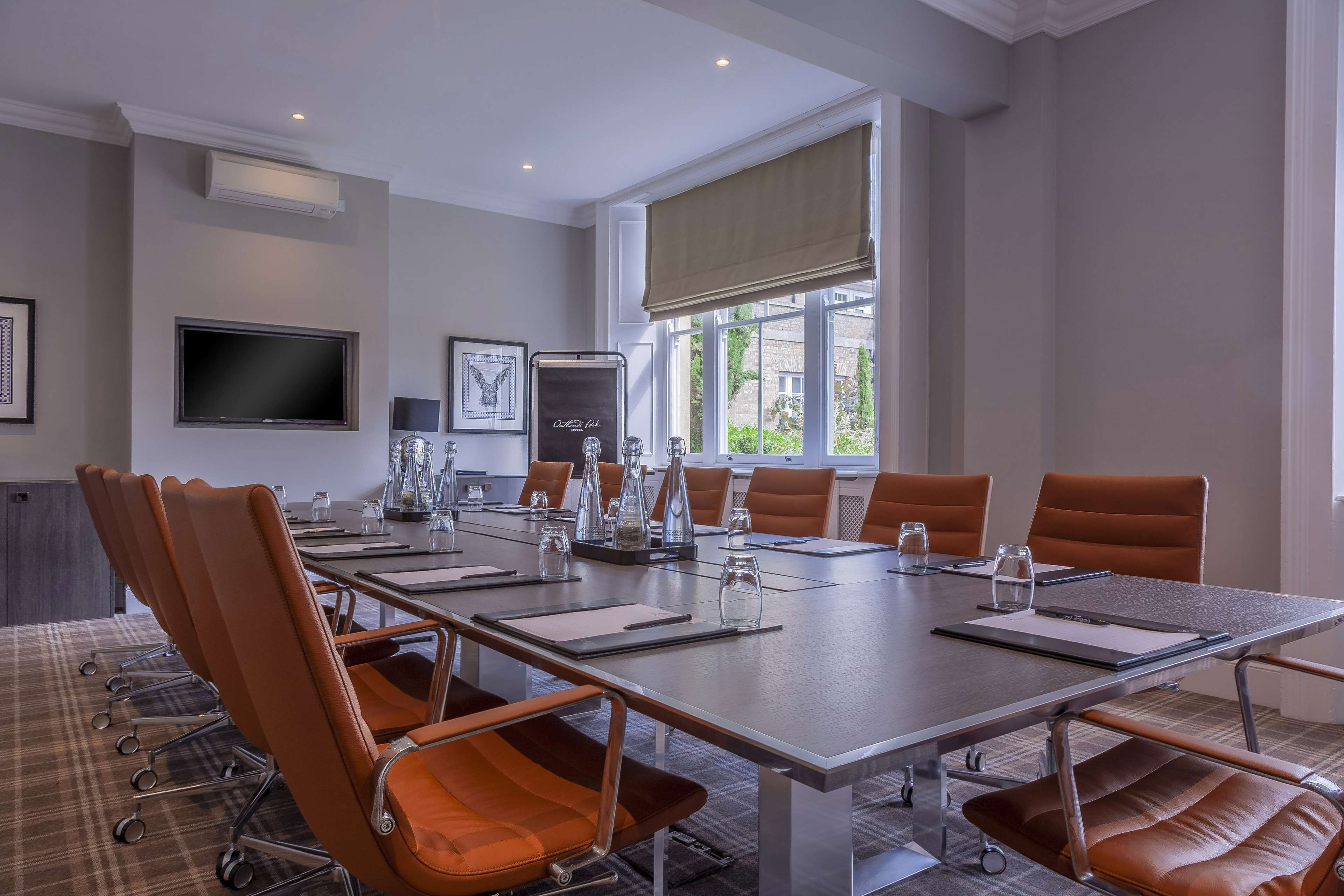 A conference room with a long table, brown leather chairs, a flat-screen TV, and a window with a view.