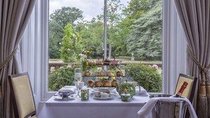 A three-tiered tea and scone stand with a view of a garden through a window. - Oatlands Park Hotel (Weybridge)