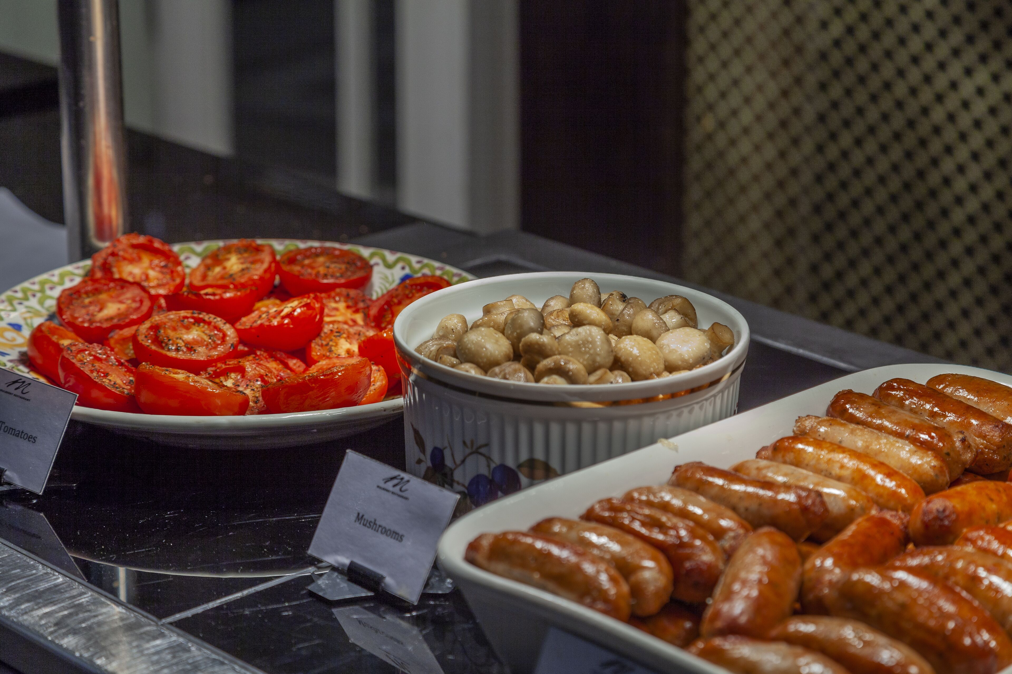 A buffet table with sliced tomatoes, mushrooms, and sausages.