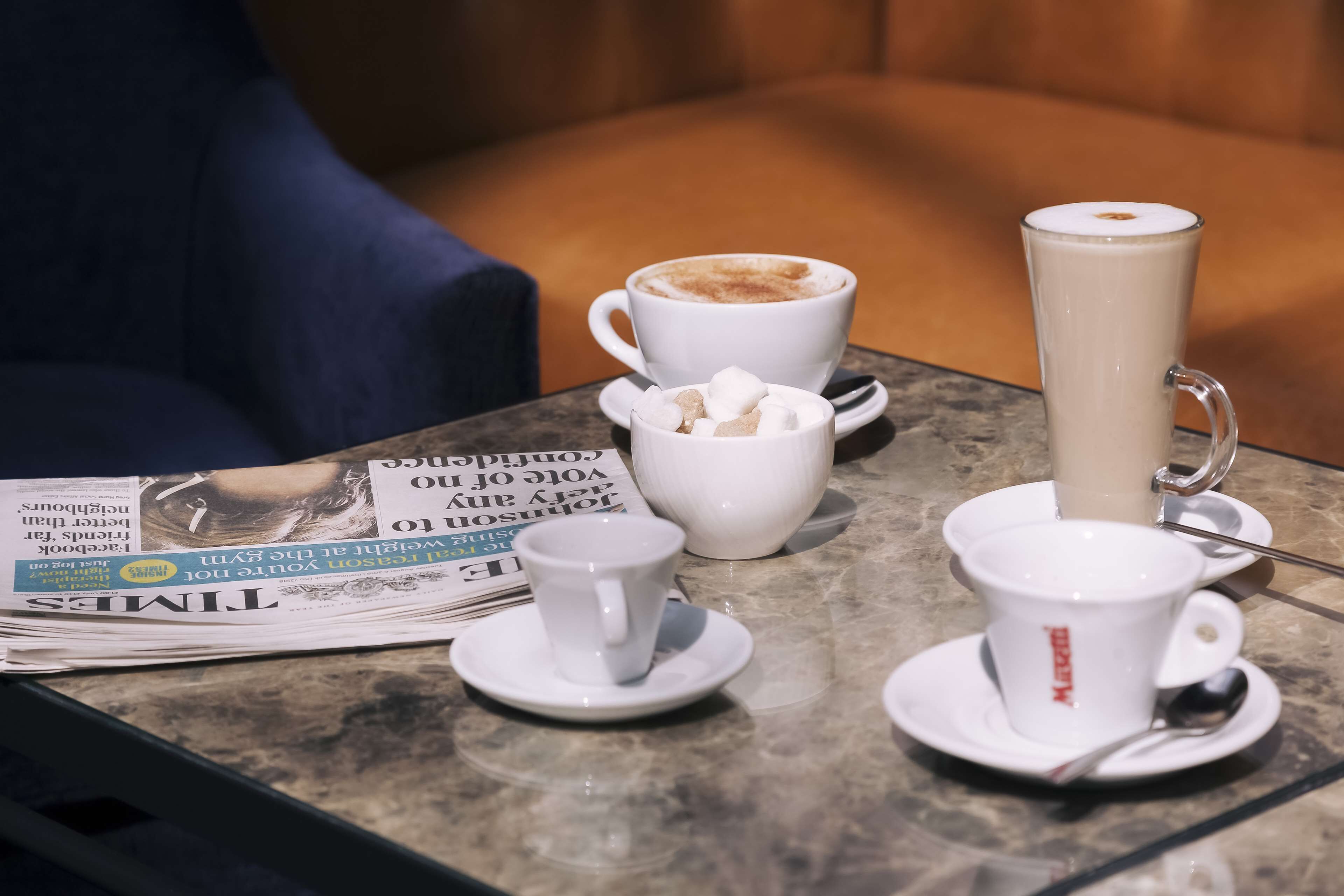 A table with a newspaper, a cup of coffee, a tall glass of milk, and a mug of hot chocolate.