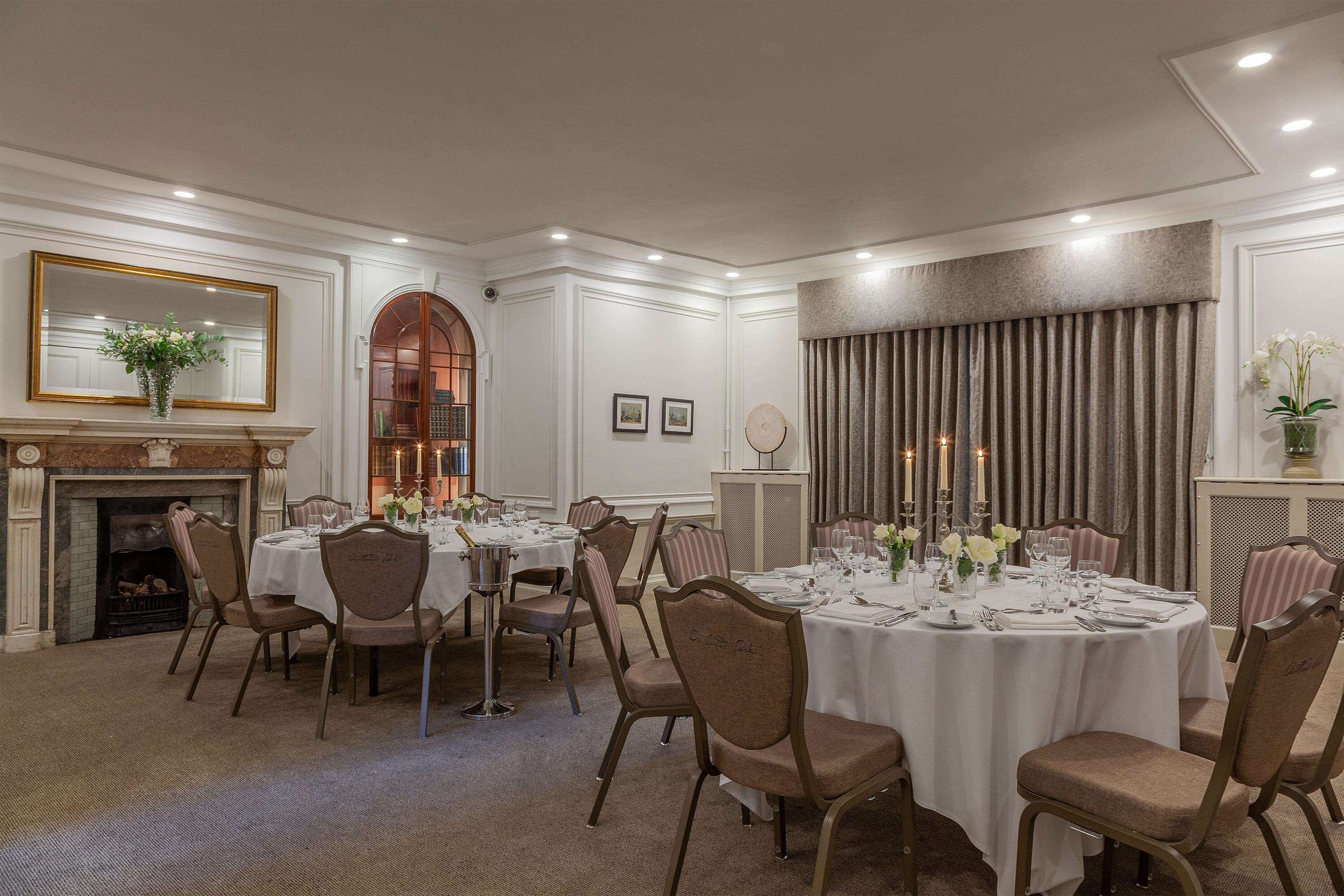 A formal dining room with round tables, chairs, and a fireplace.