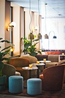 A modern lounge area with sofas, ottomans, and tables, featuring pendant lighting and potted plants.