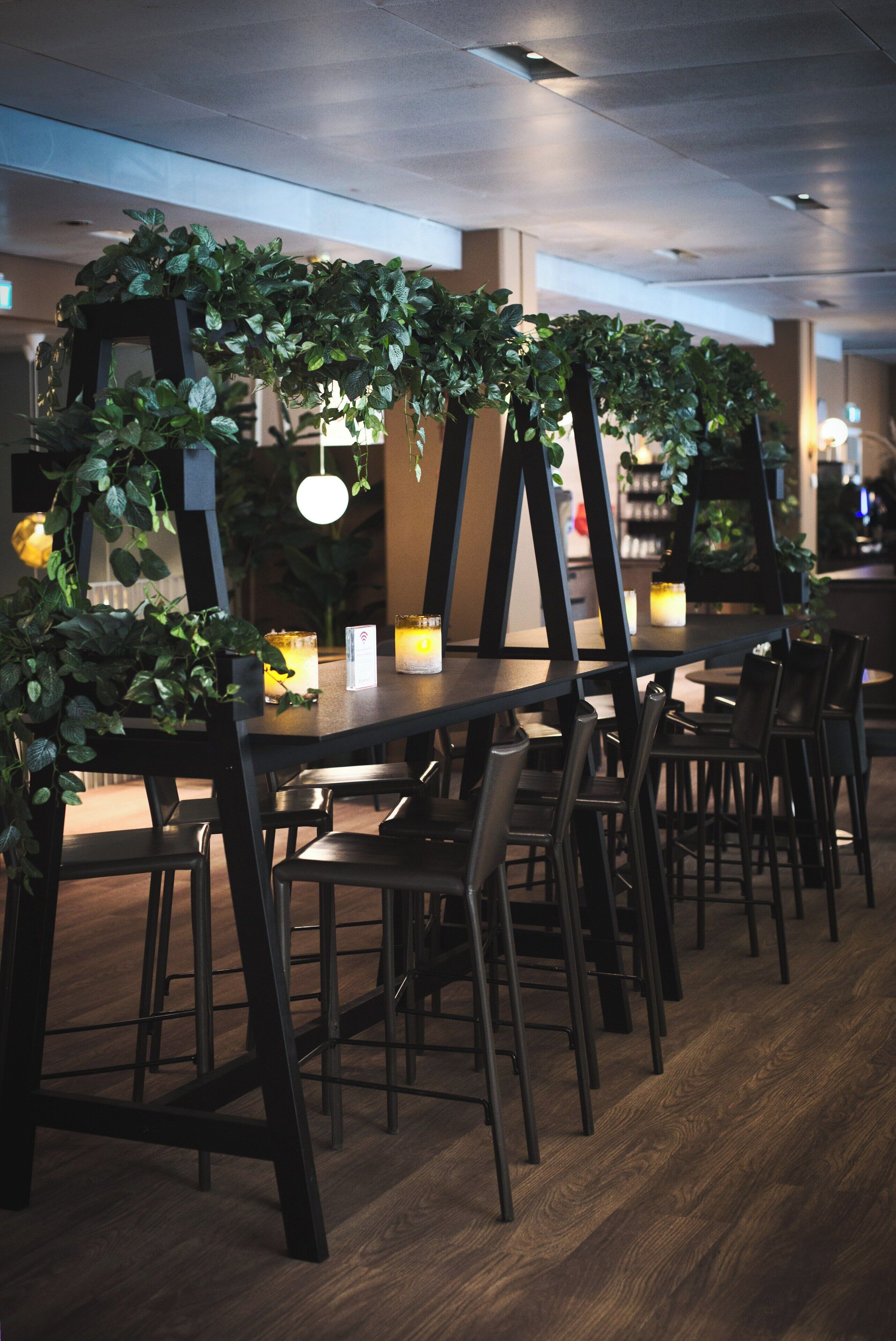 A restaurant with wooden tables and chairs, surrounded by green foliage and candles.