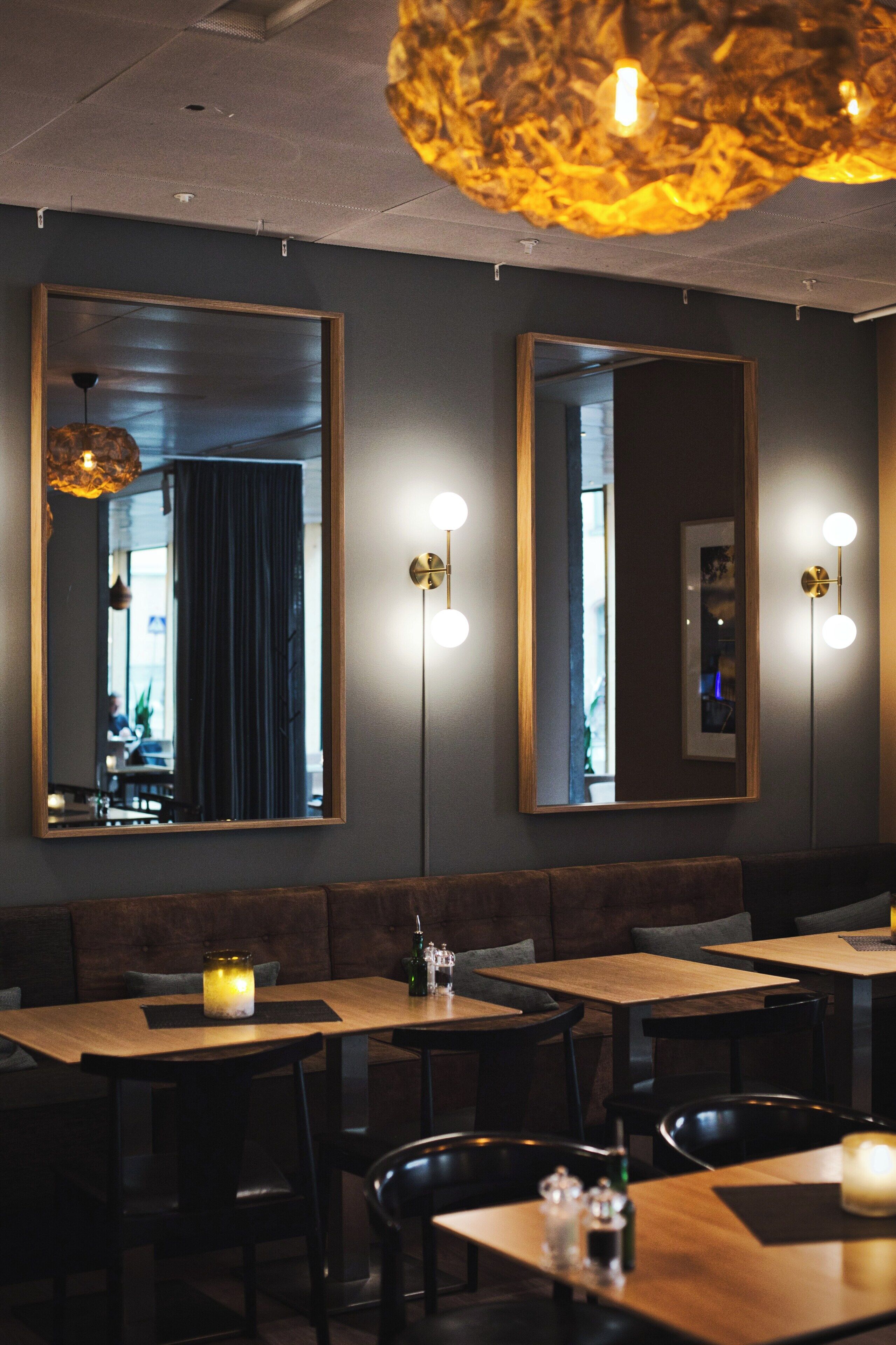 A restaurant interior with wooden tables and chairs, large mirrors on the walls, and pendant lighting.