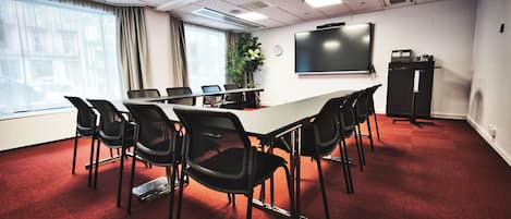 Un salón de conferencias con una larga mesa, sillas negras, una pantalla de proyector y un reloj en la pared.
