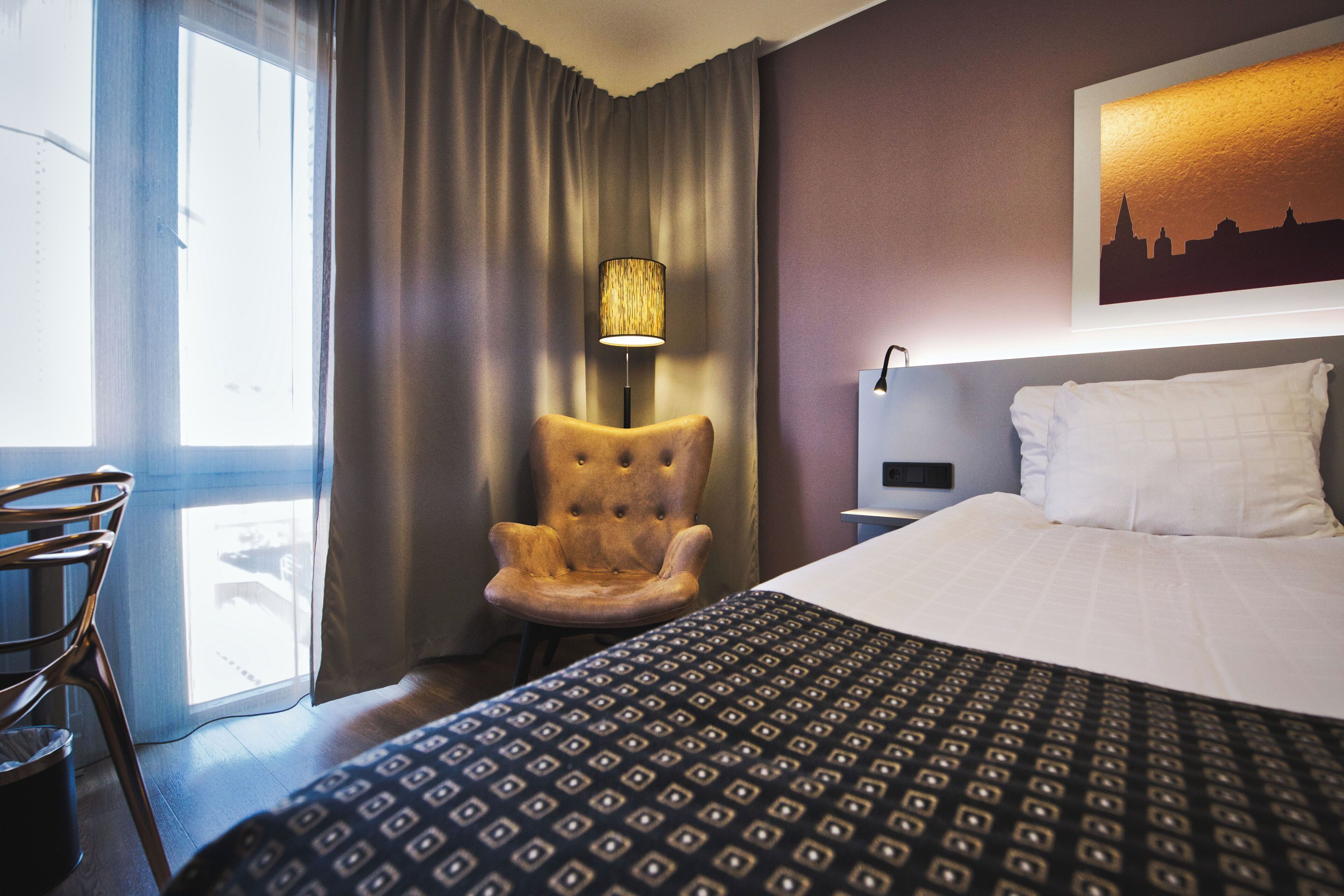 Ein Hotelzimmer mit einem Bett, einem Sessel, einer Lampe und einem Vorhangfenster.