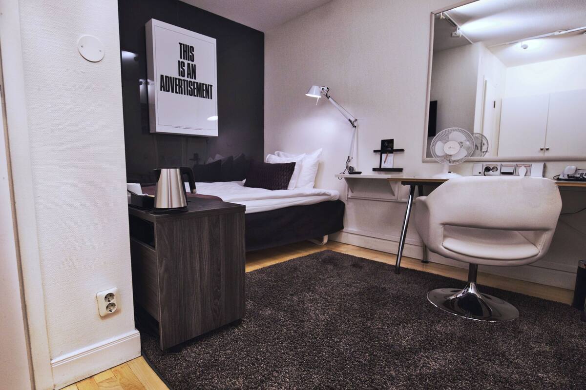 A modern hotel room with a bed, bedside table, lamp, chair, and a large mirror.