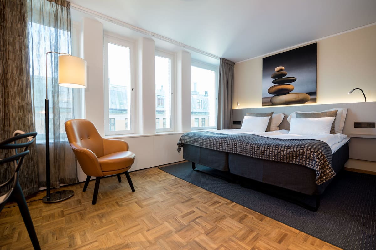 A hotel room with a bed, a chair, a lamp, and a painting on the wall.