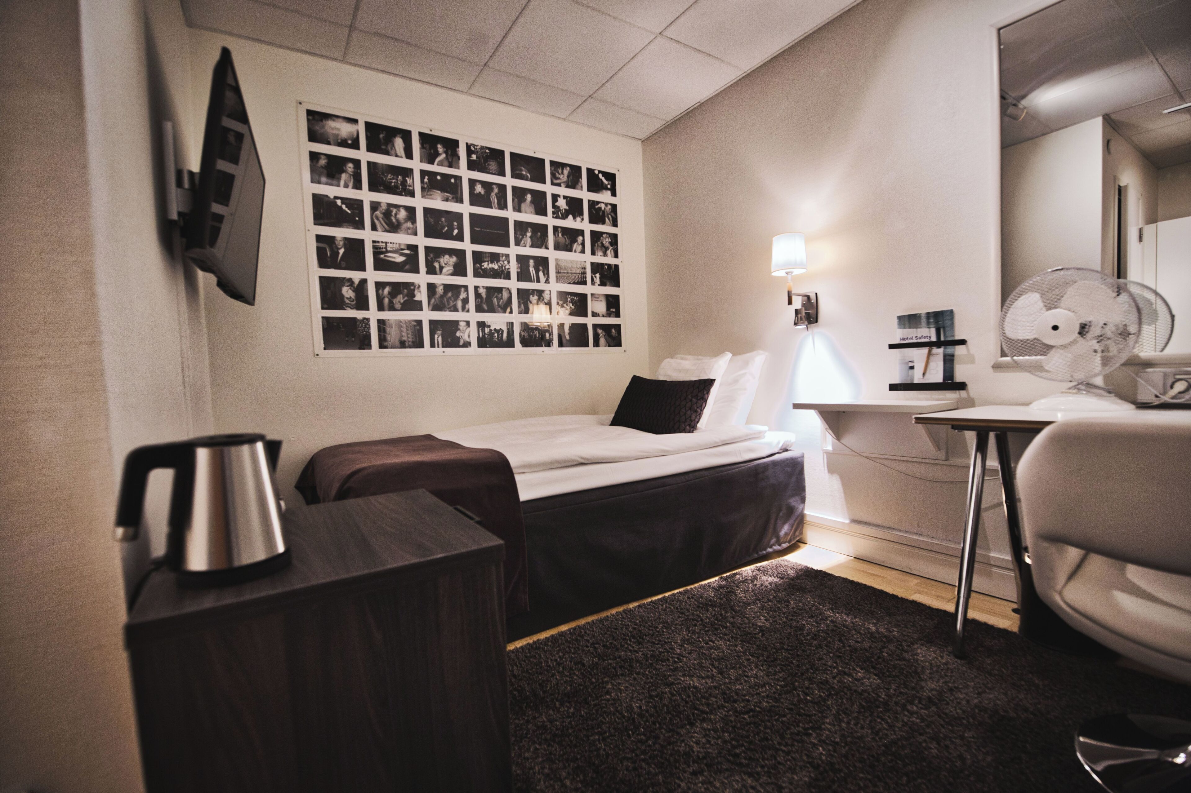 Ein Hotelzimmer mit einem Bett, einem Schreibtisch, einem Sessel, einem Wasserkocher, einem an der Wand montierten Fernseher und einer Fotowand.