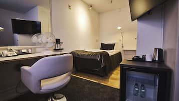 Habitación de hotel con cama, escritorio con computadora y teléfono, silla, televisor, refrigerador minibar y espejo.