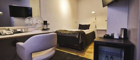 Habitación de hotel con cama, escritorio con computadora y teléfono, silla, televisor, refrigerador minibar y espejo.