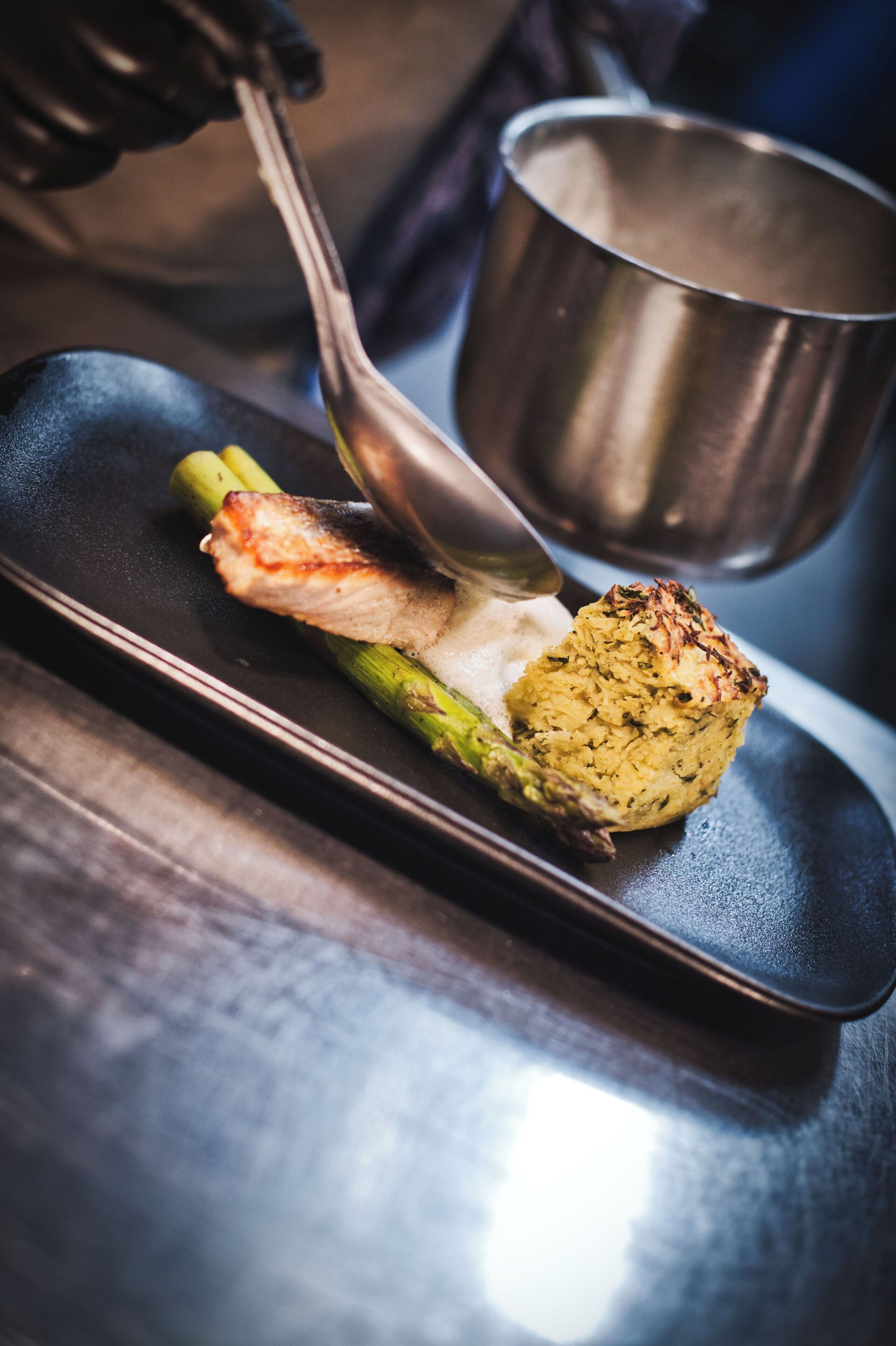 A close-up of a dish with grilled asparagus and a mound of rice topped with herbs, served on a black plate.