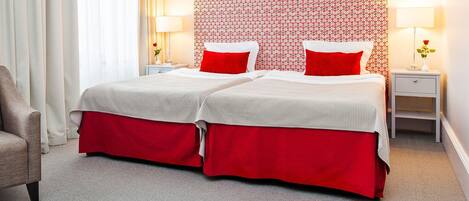 A double bed with red bedding, two bedside tables with lamps, and a chair.