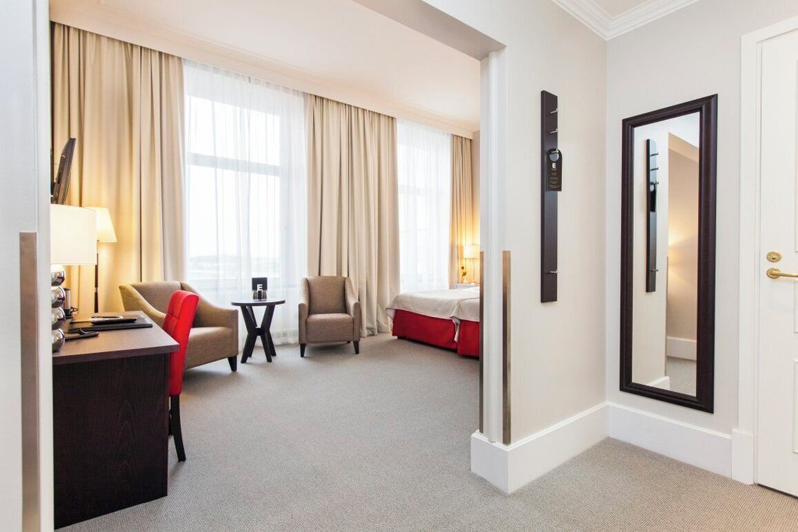 A hotel room with a desk, two chairs, a bed, and a large mirror.