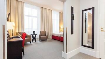 A hotel room with a desk, two chairs, a bed, and a large mirror.