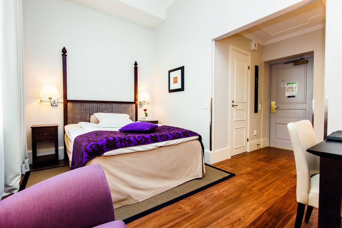 Habitación de hotel con cama, mesitas de noche, una silla y una puerta.