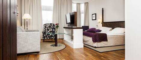 A hotel room with a sofa, a bed, a TV, and a desk with a lamp.