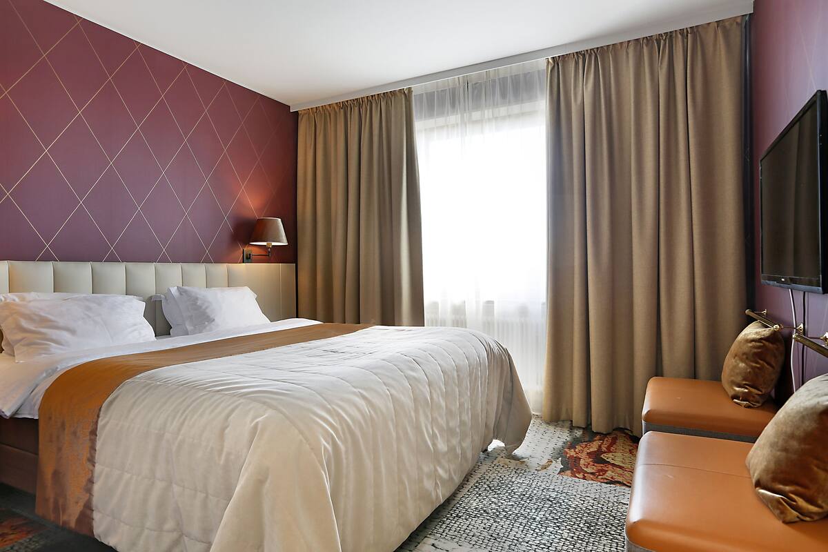 Habitación de hotel con una cama grande, un sofá, un televisor y una ventana con cortinas.