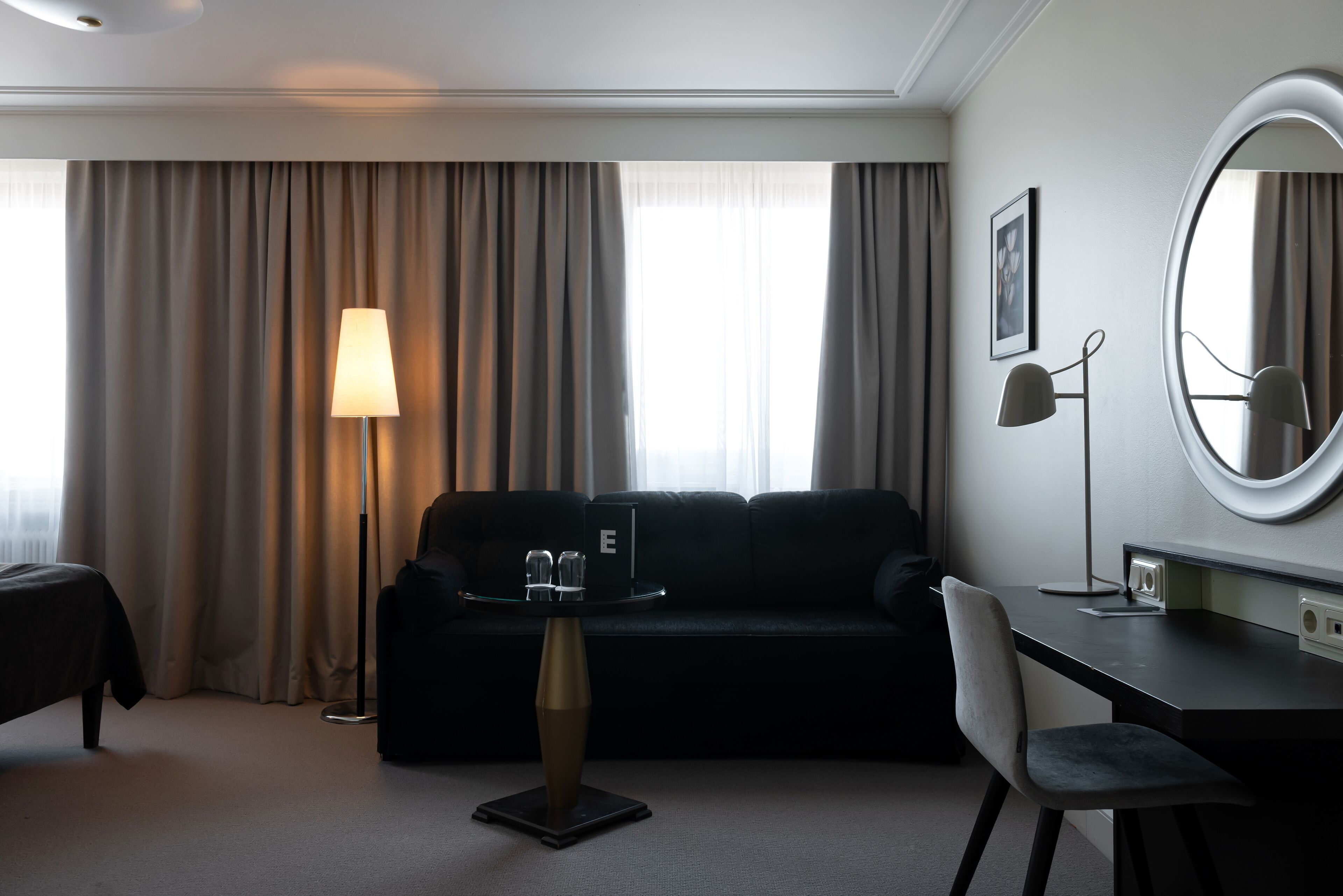 A hotel room with a bed, a desk, a chair, a lamp, a sofa, and a large mirror.