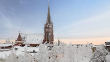 Una iglesia con una aguja alta y una torre del reloj, rodeada de árboles y edificios cubiertos de nieve.