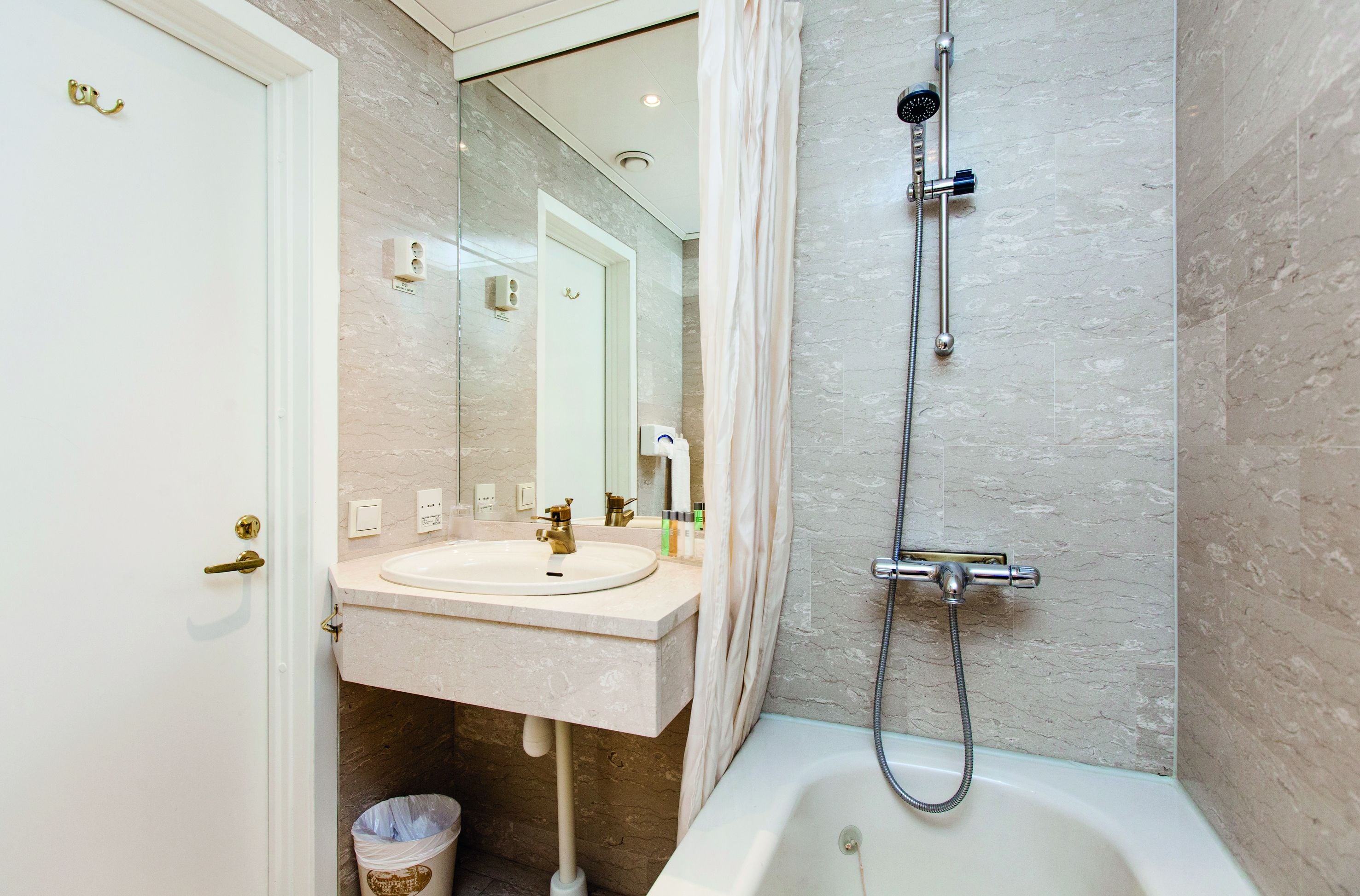 A bathroom with a sink, mirror, shower, and a trash bin.