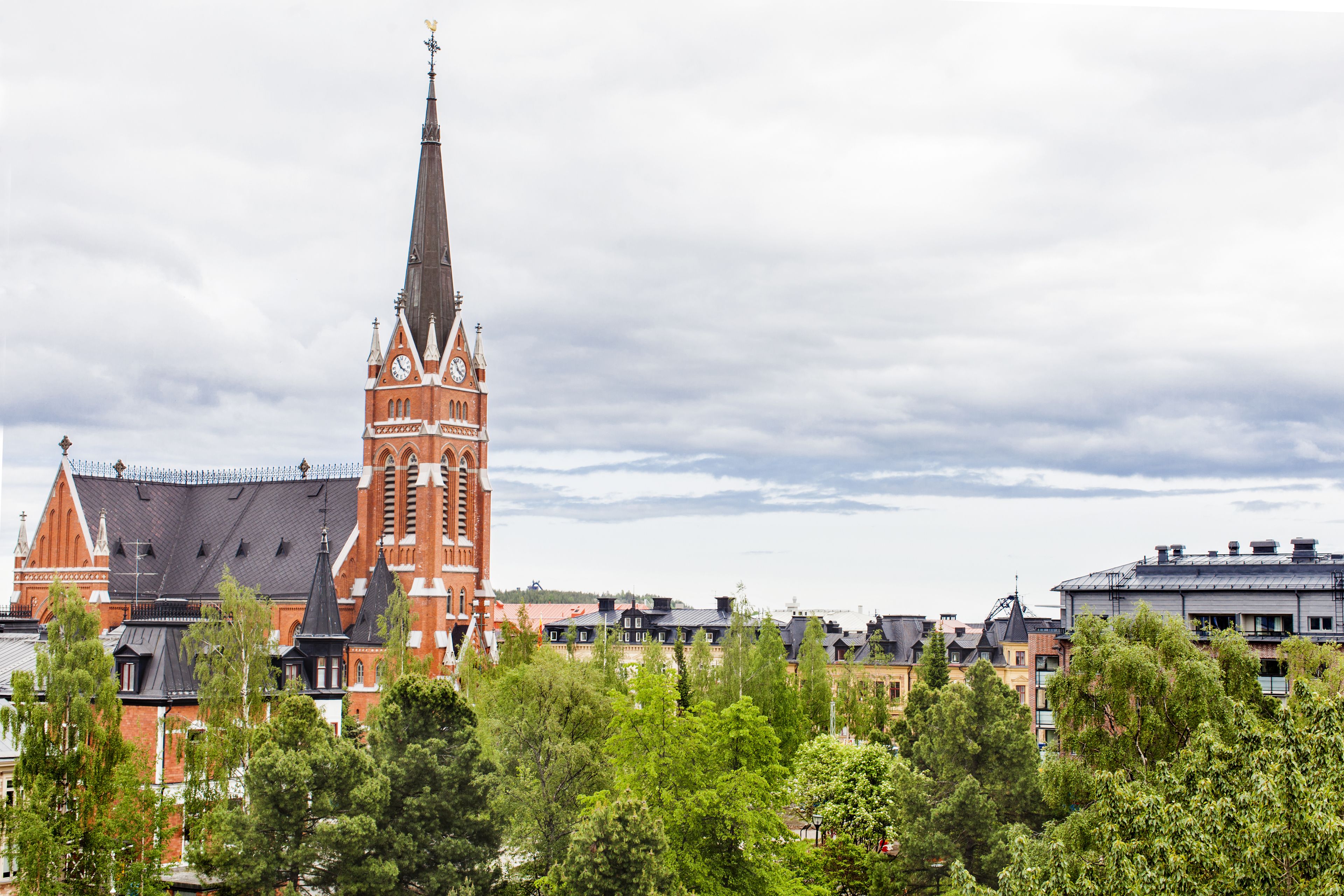A historic church with a tall spire and a clock tower, surrounded by trees and modern buildings.