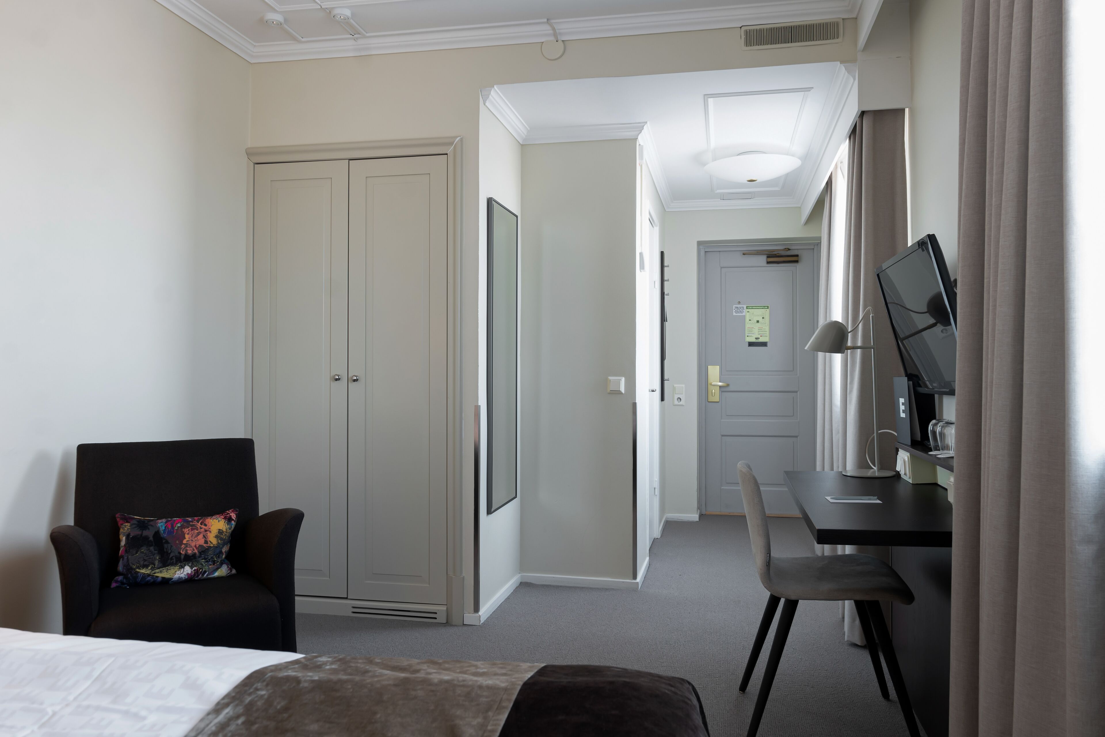 A hotel room with a bed, a desk, a chair, a TV, and a wardrobe.
