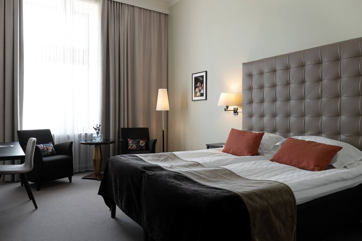 Una habitación de hotel con una cama grande, un escritorio, una silla y una lámpara.