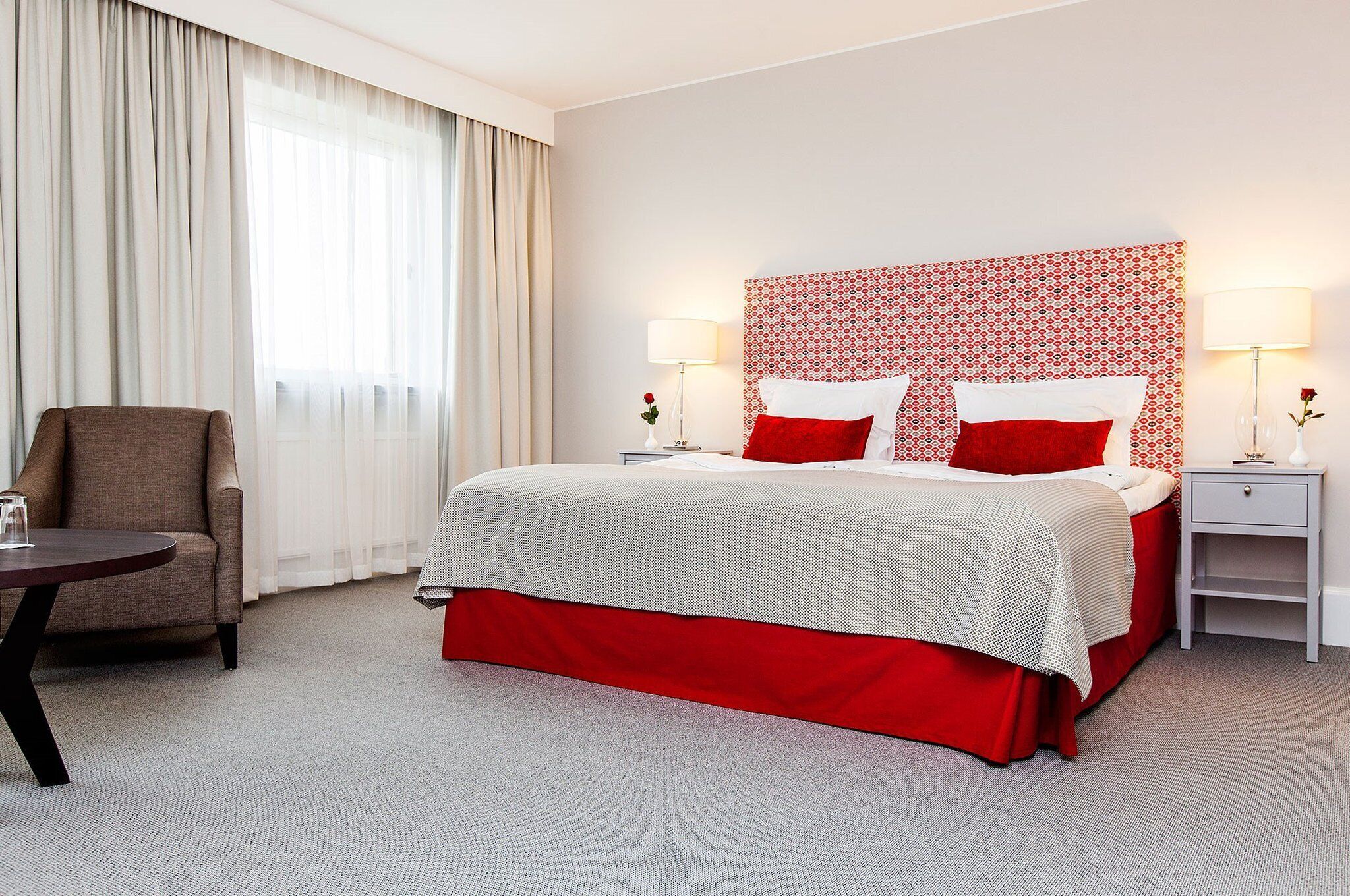 A hotel room with a bed, a chair, a nightstand, and a lamp.