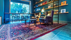 A modern living room with a large window, a patterned rug, leather armchairs, and a bookshelf filled with books and framed pictures. - Scandic Stortorget (Malmö)