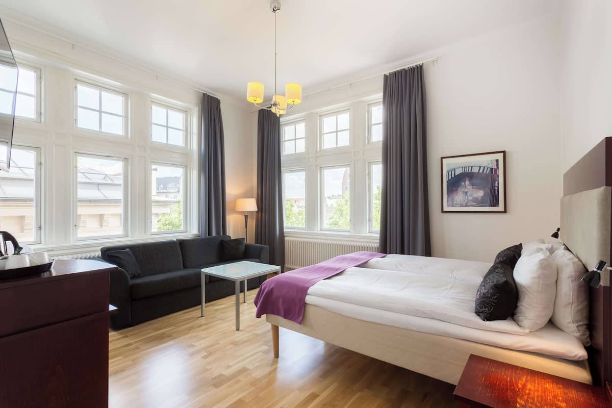 A hotel room with a bed, a sofa, a coffee table, and a desk.