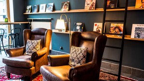A room with two leather armchairs, a bookshelf with various books, a radiator, and a lamp. - Scandic Stortorget (Malmö)