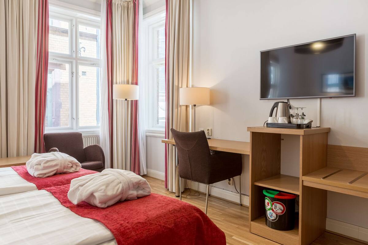 A hotel room with a bed, two chairs, a desk, a TV, and a coffee machine.