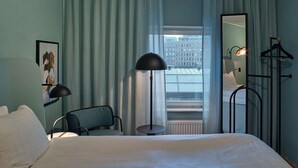 A hotel room with a bed, a chair, a table, a mirror, and a view of buildings through the window. - Scandic Klara (Stockholm)
