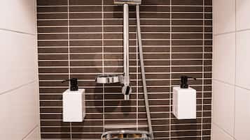 Une douche équipée d’un pommeau de douche à main et d’un pommeau de douche fixe fixé au mur, tous deux reliés par des tuyaux. Deux distributeurs de savon blancs sont fixés au mur.