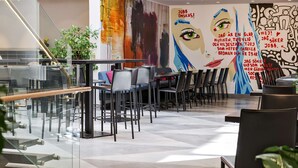 A modern restaurant interior with glass railings, black and grey chairs, and a colorful mural on the wall. - Scandic Klara (Stockholm)