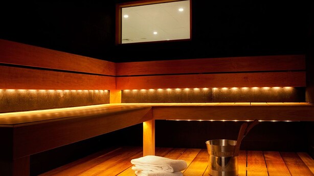 A sauna with wooden benches, a window, and a bucket on the floor. - Scandic Klara (Stockholm)