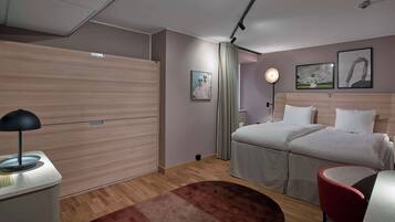 A modern hotel room with a bed, bedside table, lamp, and a red chair.
