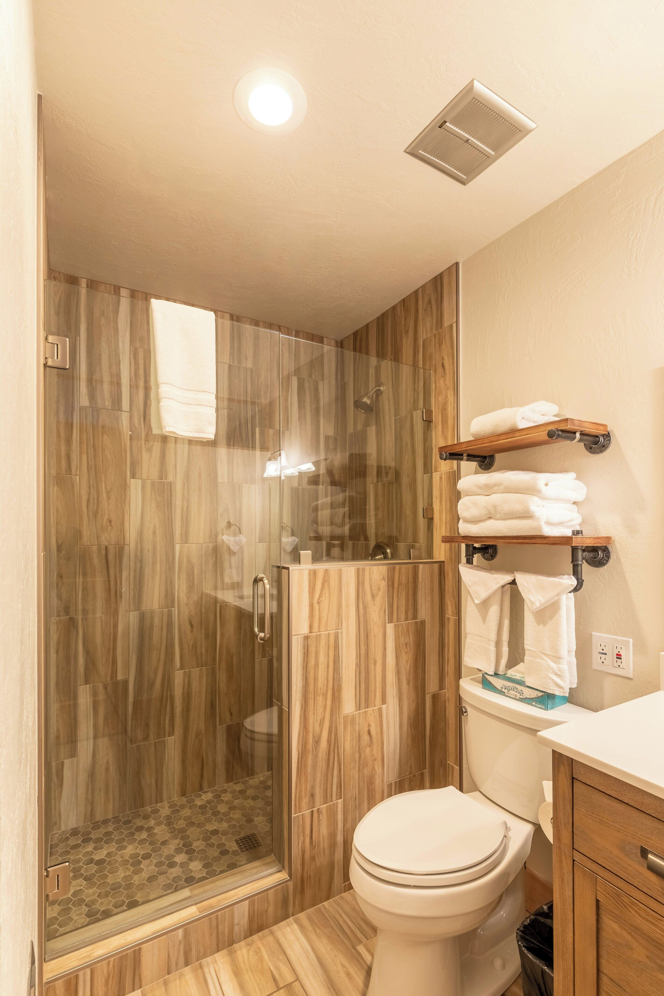 Un baño moderno con ducha envuelta en vidrio, inodoro y suelo de madera.