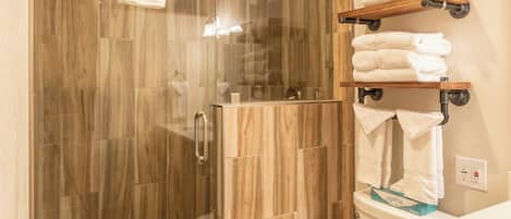 Un baño moderno con ducha envuelta en vidrio, inodoro y suelo de madera.
